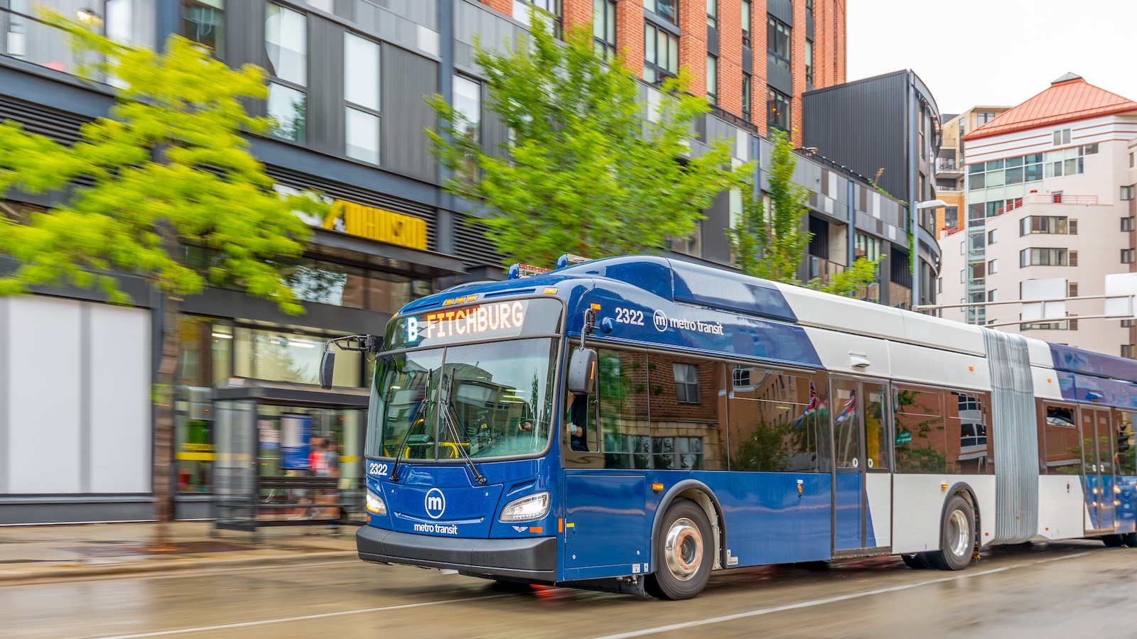 60' electric bus rolling down street with shops 